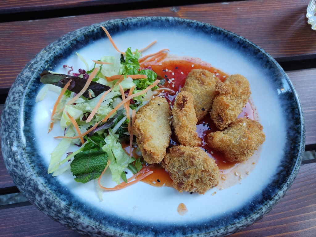 Six crispy nuggets with a fresh side salad sitting in a bright orange spicy sauce