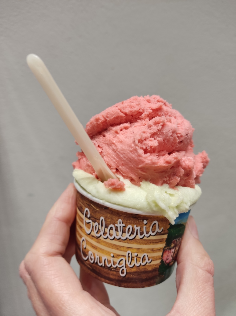 A cup of ice cream with a scoop of pale basil and lemon topped by a pastel pink scoop of strawberry