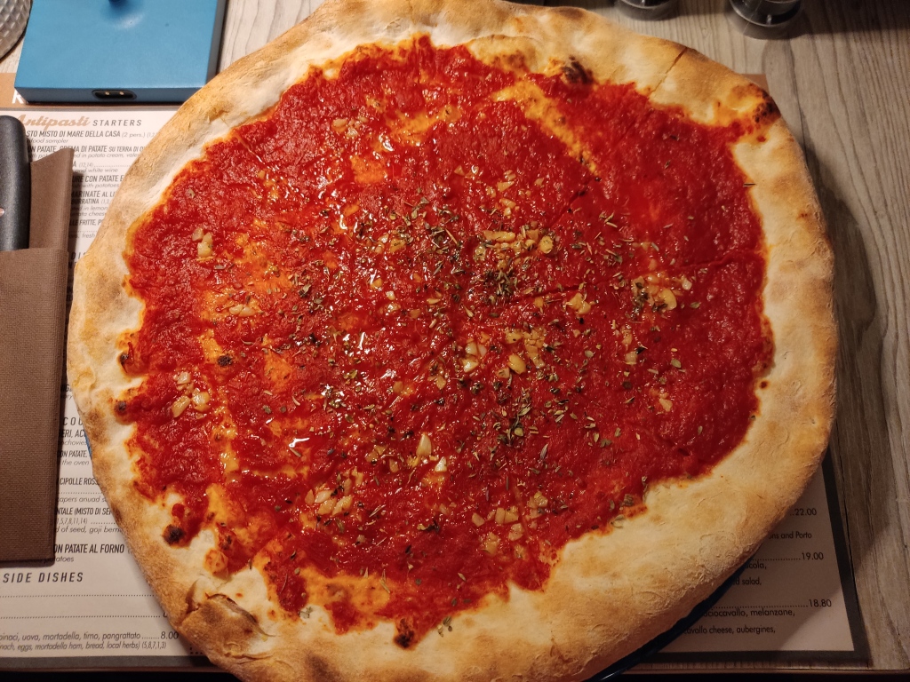 A large pizza topped with tomato sauce and lots of chopped garlic and herbs.